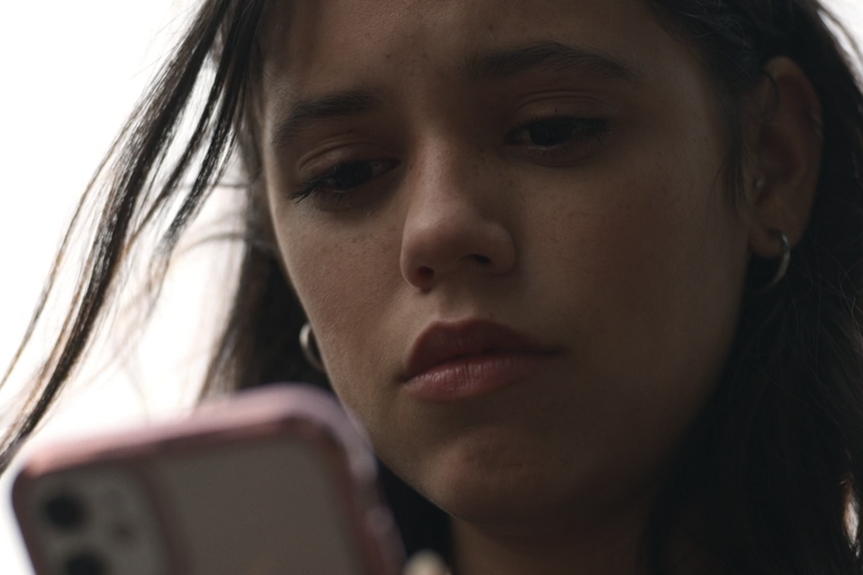 A girl with brown hair looks down at her cell phone.