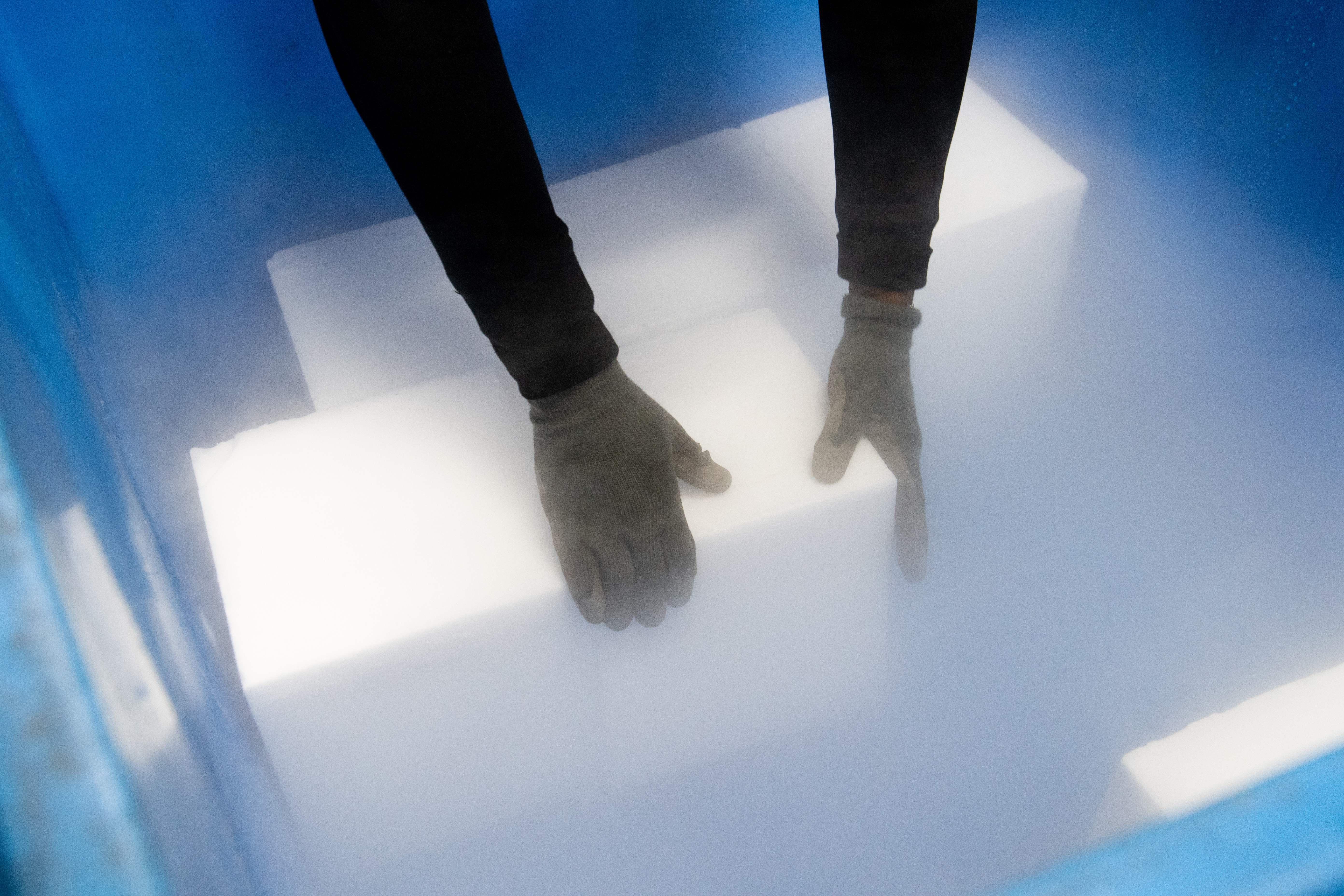 Gloved hands reach inside a cooler to place blocks of dry ice