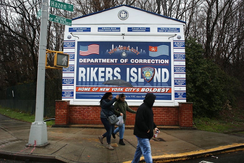 People walk by a sign at the entrance to Rikers Island.