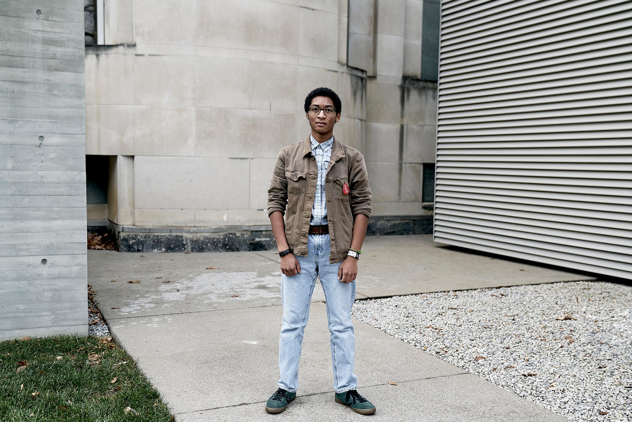 Shawn, standing outdoors on the sidewalk near a concrete building, 10th grade.