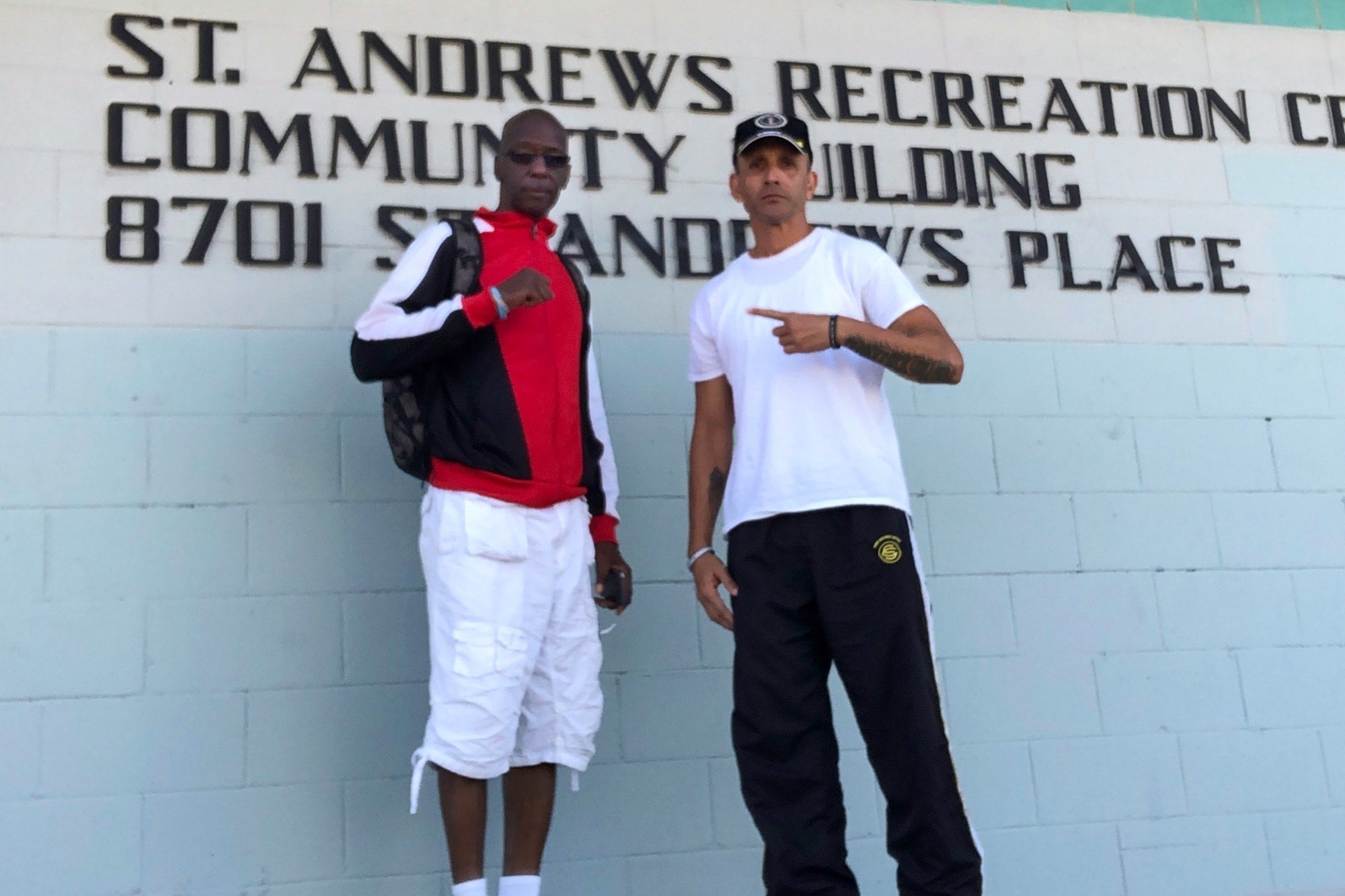 Two men stand in front of a sign that says St. Andrews Recreation Center Community Building.