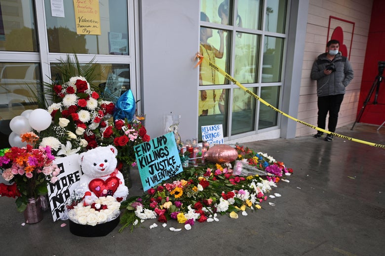 Flowers, signs, and teddy bears in an area roped off by caution tape in front of a store.