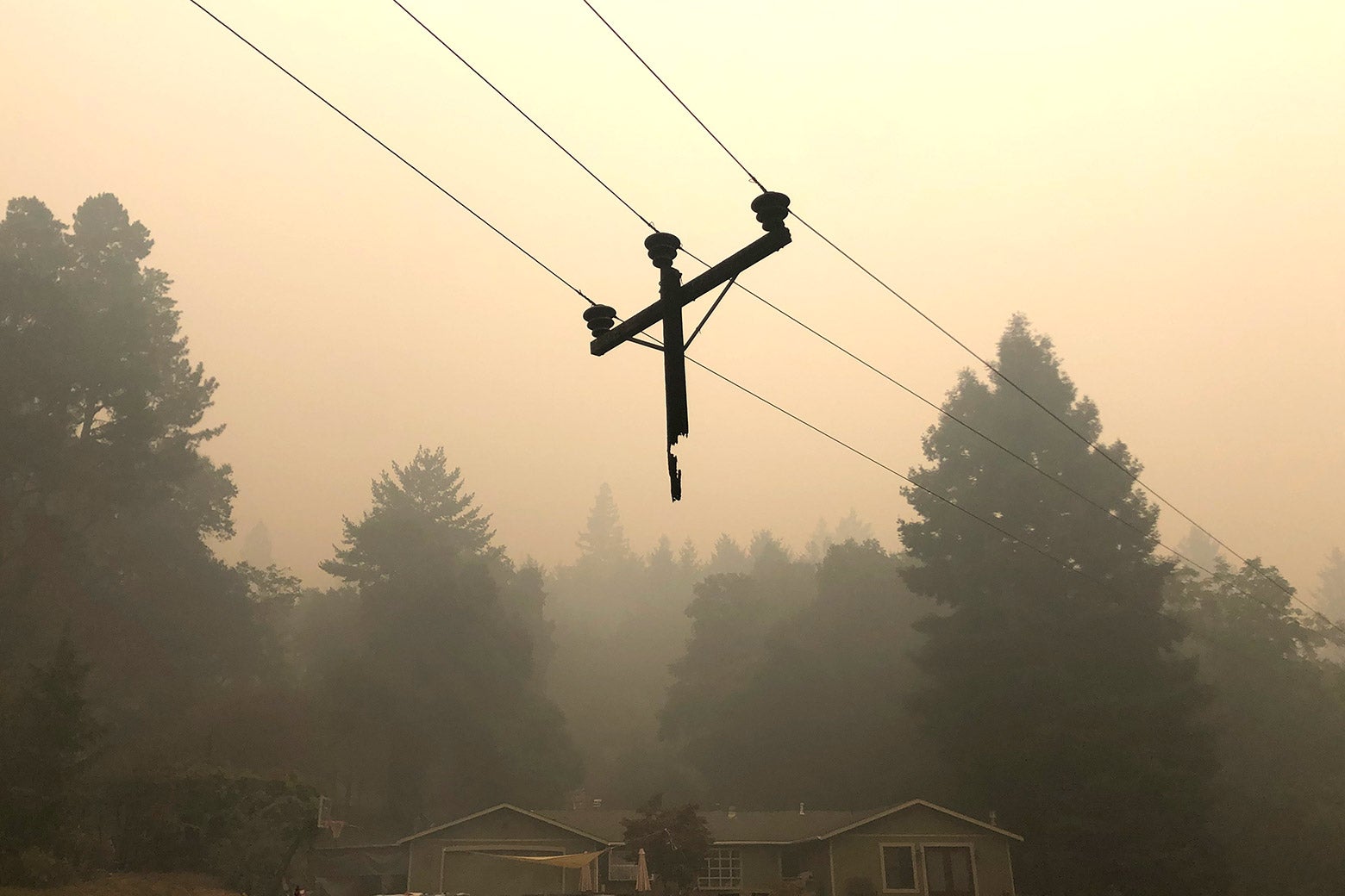Just the top of a utility pole dangles from wires in an area filled with smoke