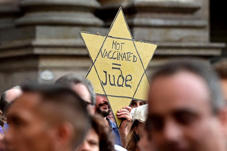 A protester in a crowd holding a yellow star that reads "Not Vaccinated = Jew"