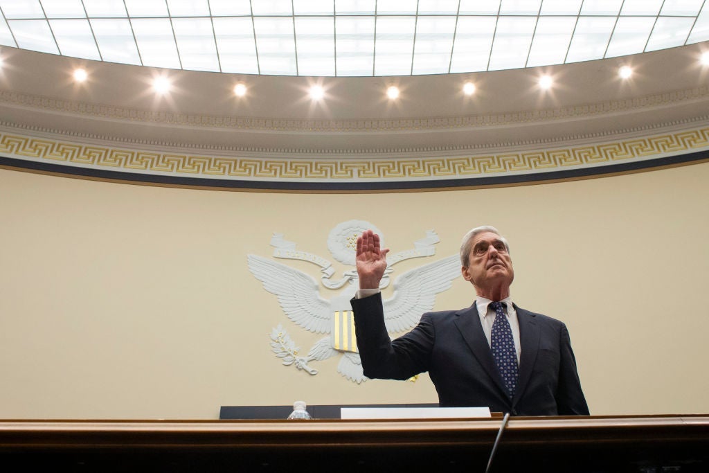 Robert Mueller, pictured against a wall emblazoned with the United States seal, holds up his right hand.