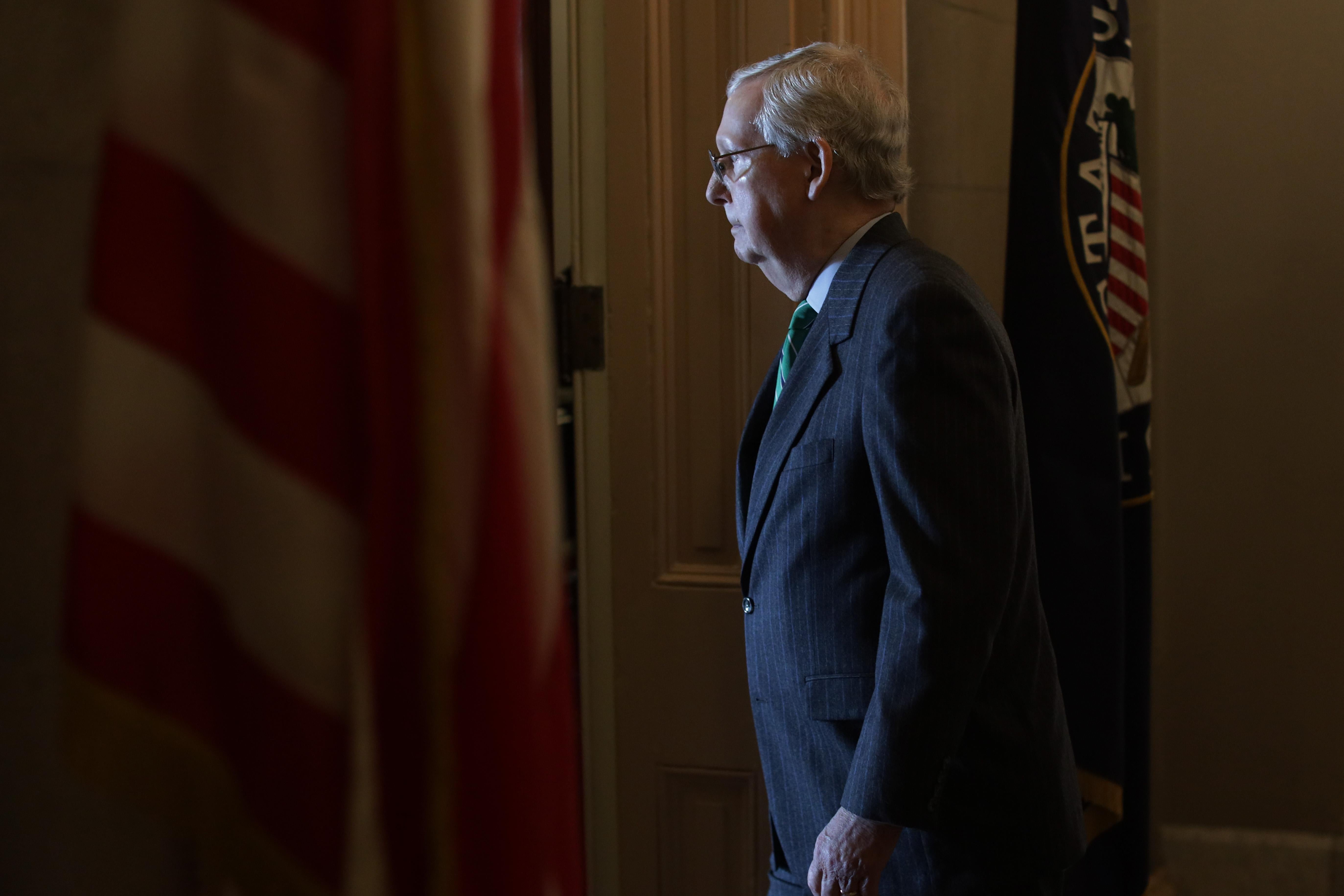 Mitch McConnell walks in a room with an American flag.