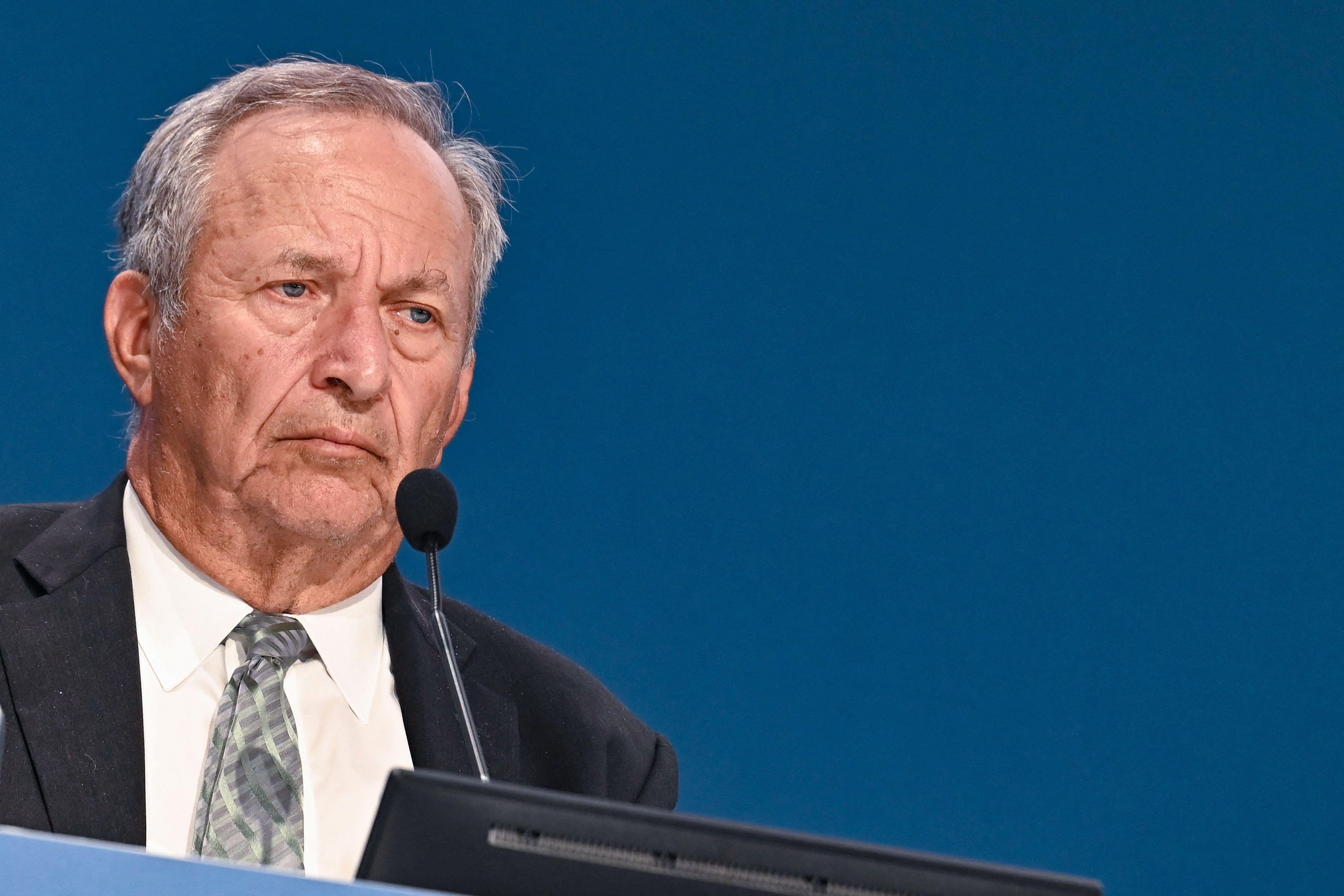 Larry Summers appears in front of a microphone, stern look on his face.