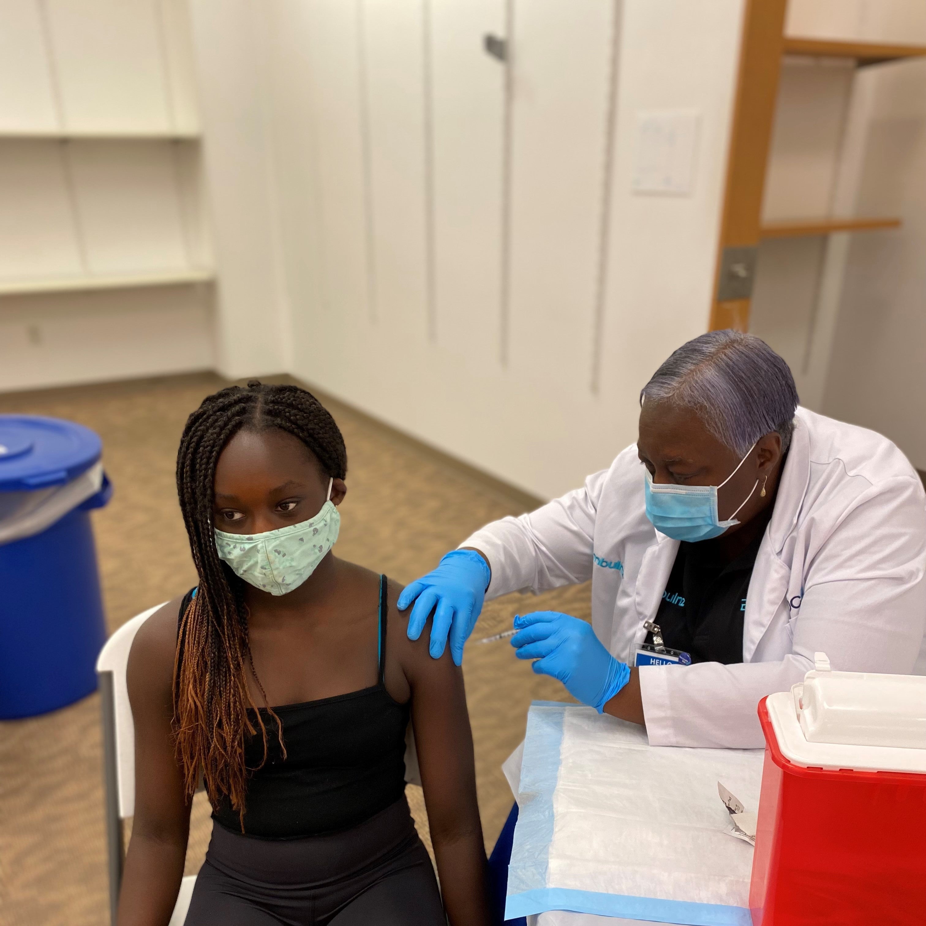 A masked girl sitting next to a table receives a vaccine.