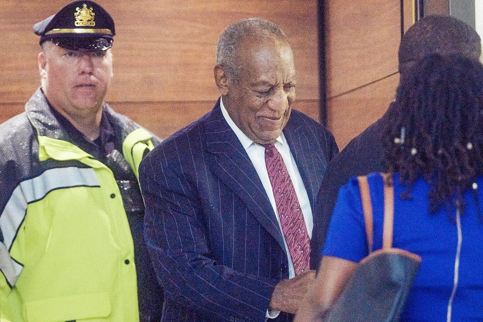 Bill Cosby smiles as he steps out of an elevator at the courthouse wearing a suit.