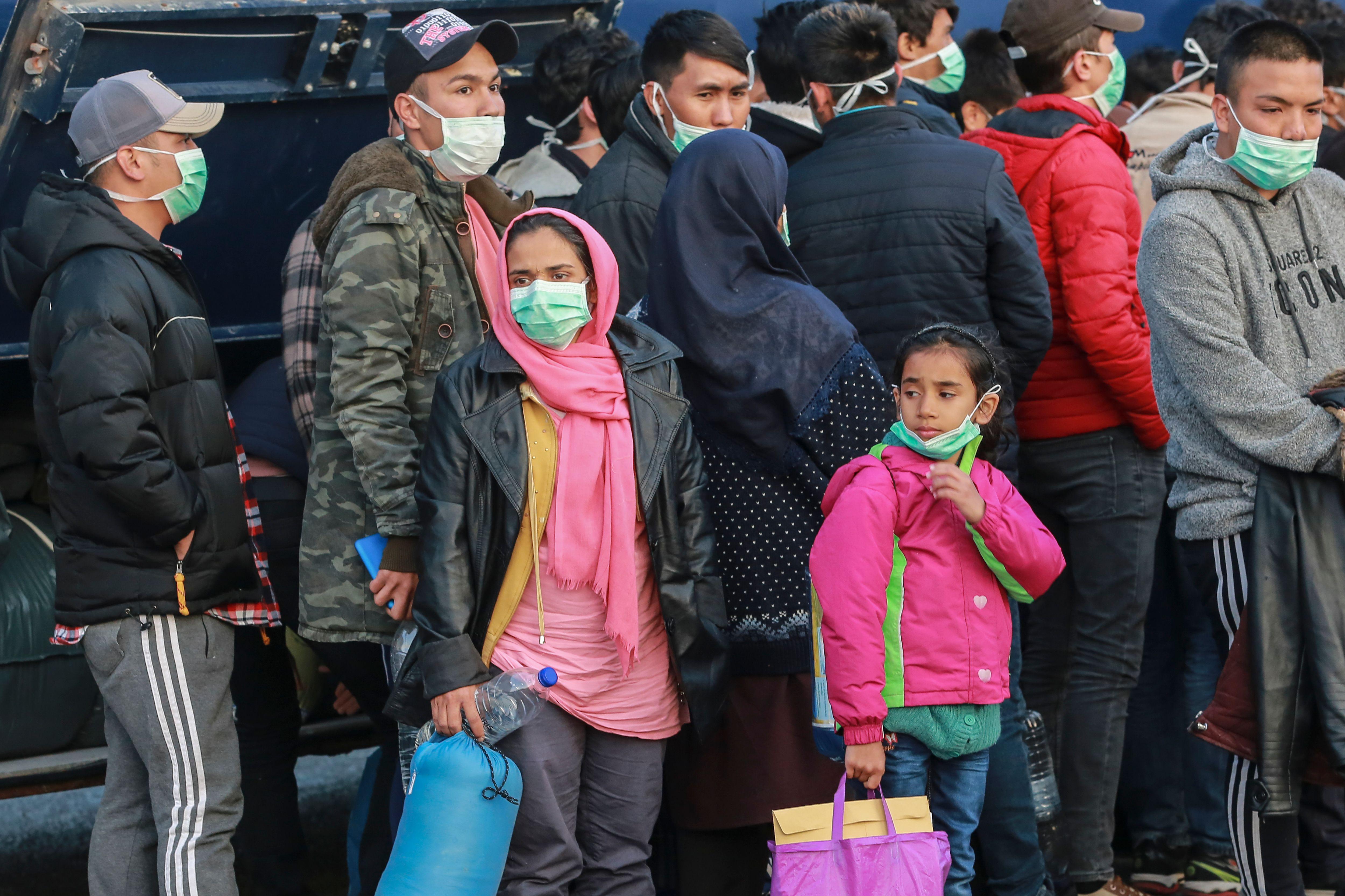 Refugees stand in line wearing masks.