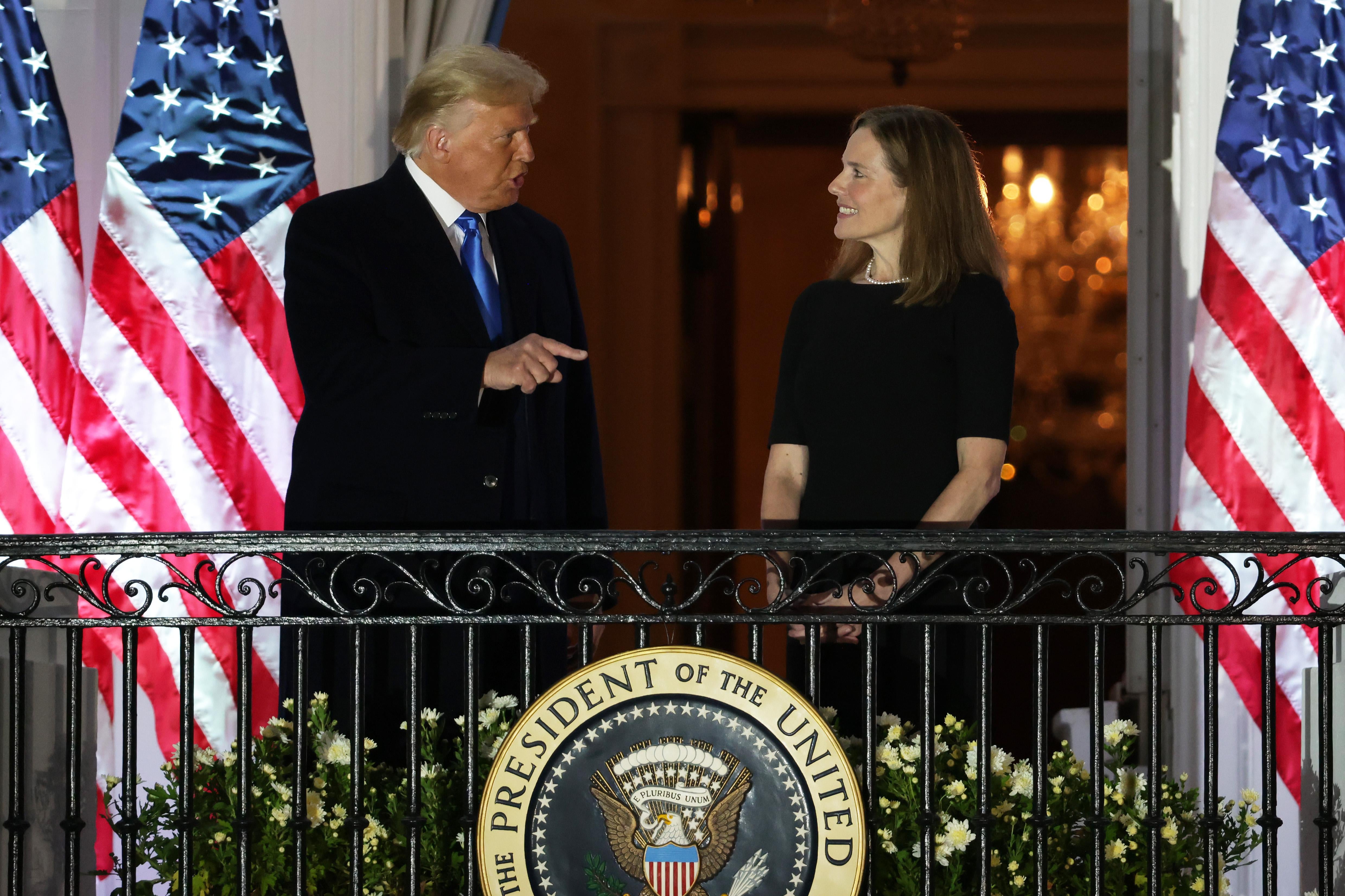 Donald Trump points as he speaks with Amy Coney Barrett on a White House balcony.