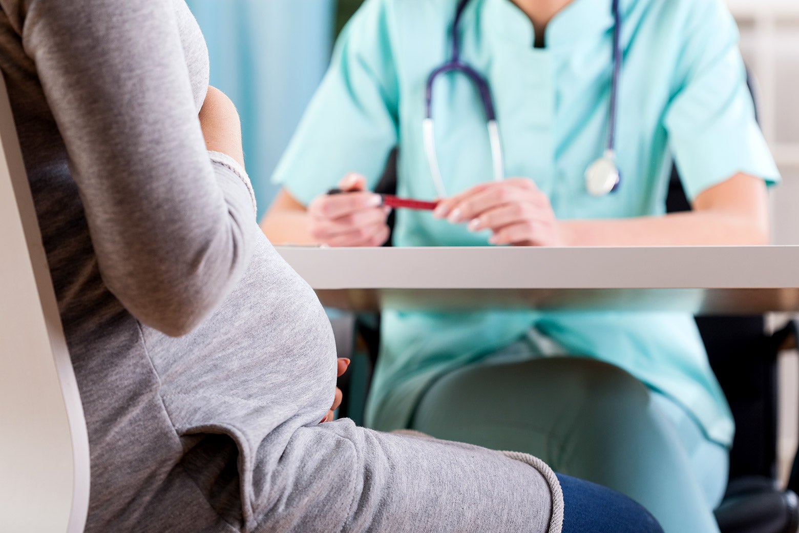 A pregnant woman holding her stomach while she speaks to a doctor.