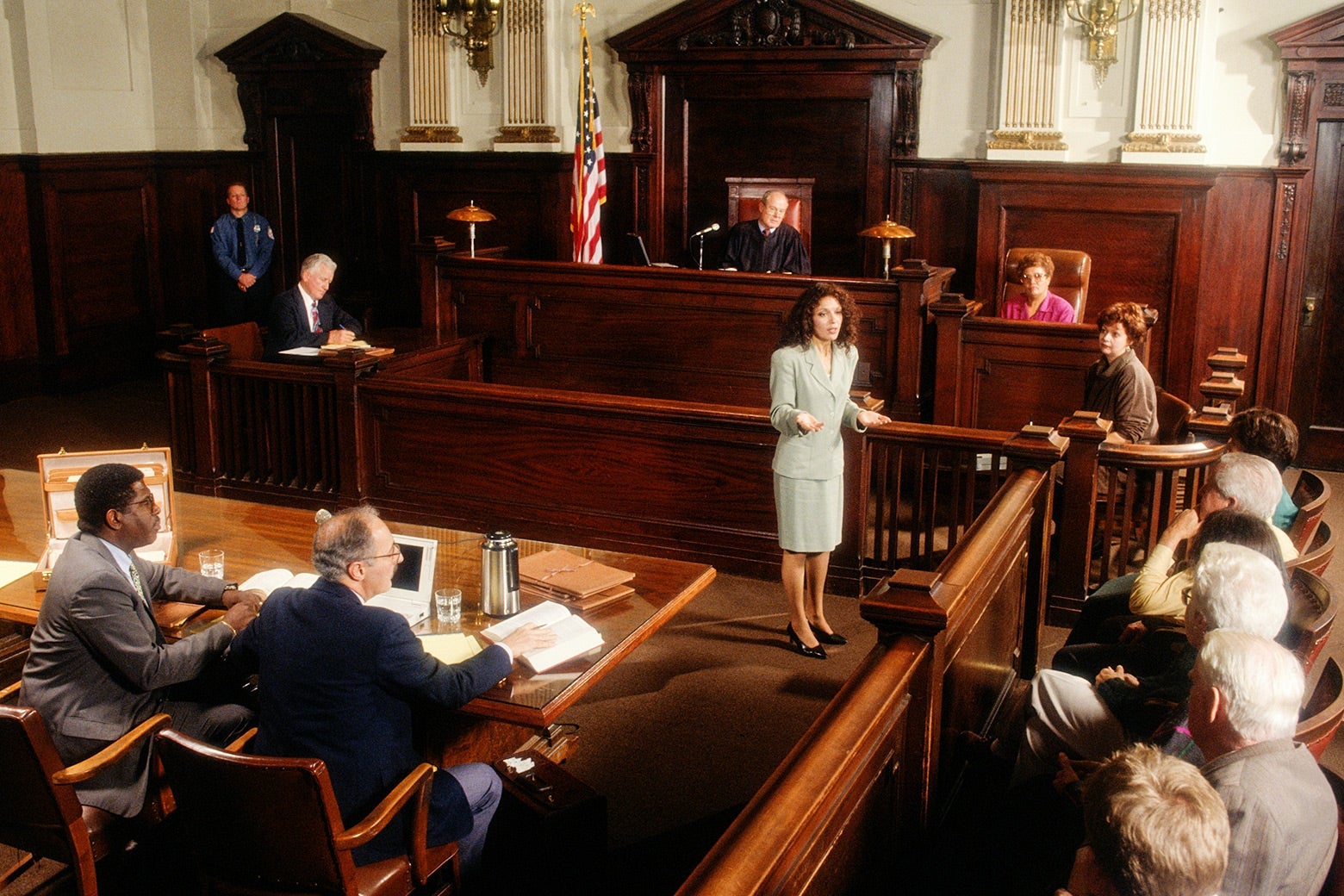 A female prosecutor stands and speaks to the jury in a courtroom