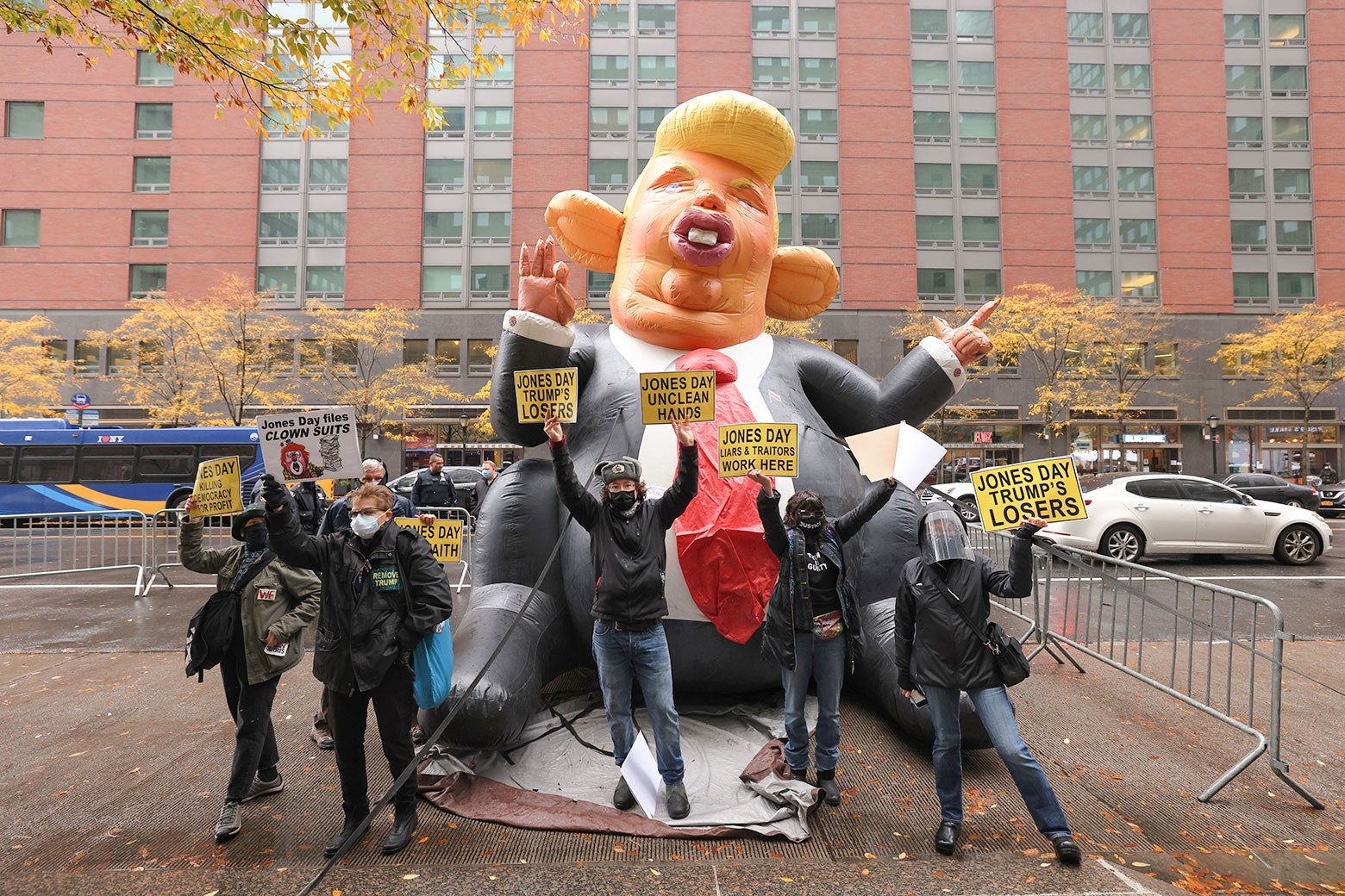 People hold up signs that say, "Jones Day Trump's Losers" in front of a large inflatable rat that looks like Donald Trump.