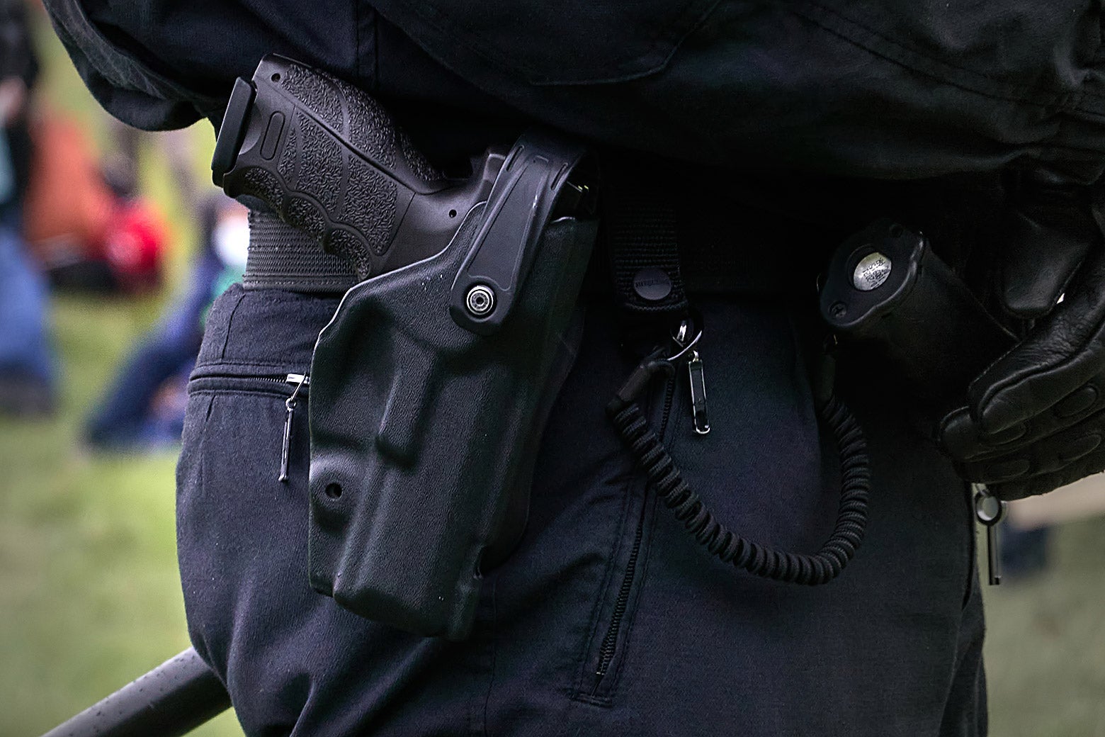 A pistol in the holster of a uniformed police officer wearing leather gloves.