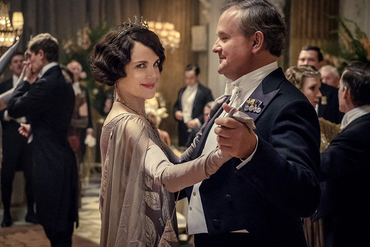 Elizabeth McGovern gives the camera a sly smile while dancing with Hugh Bonneville in a still from Downton Abbey.