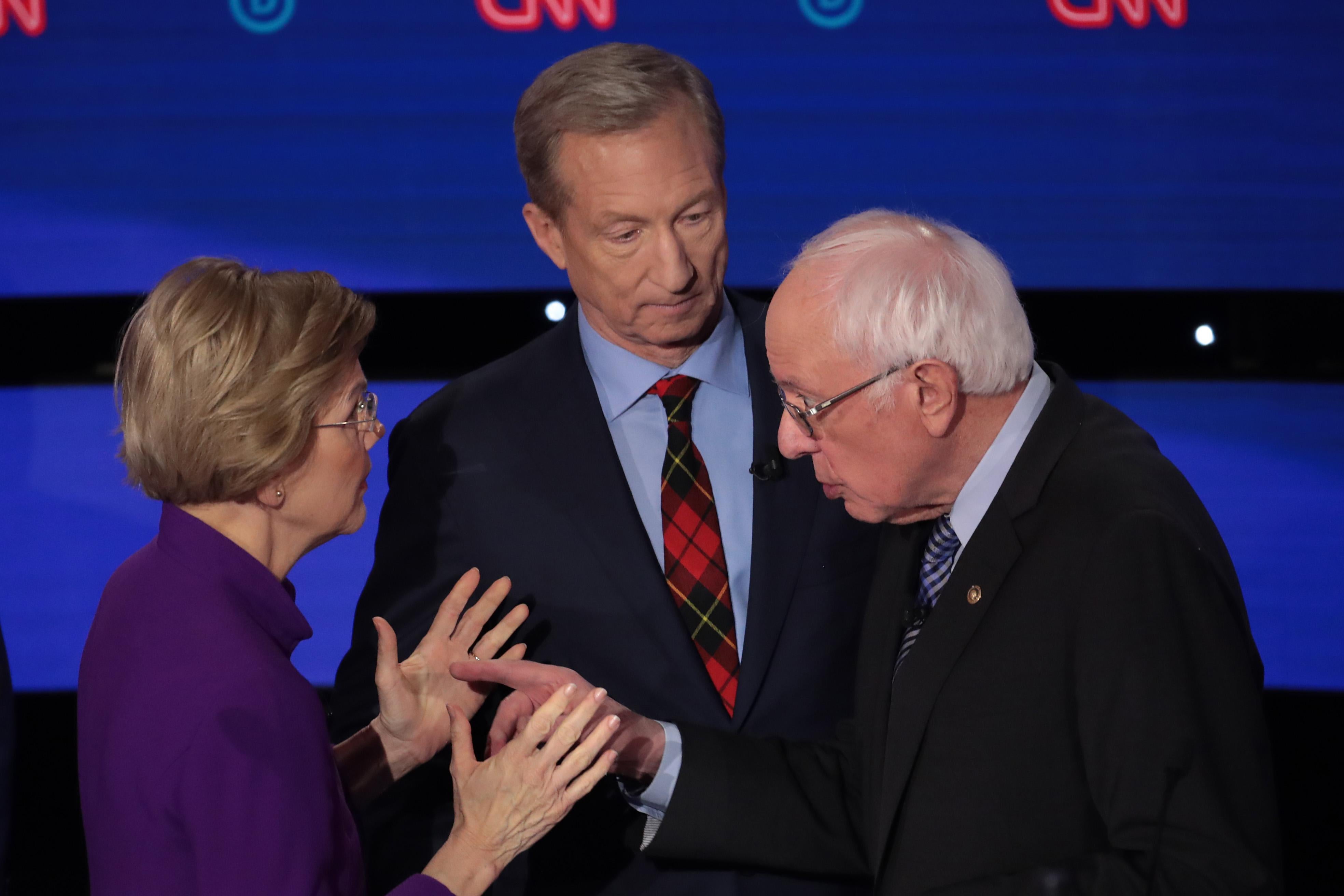 Elizabeth Warren and Bernie Sanders face each other in a heated conversation onstage as Tom Steyer looks on beside them.