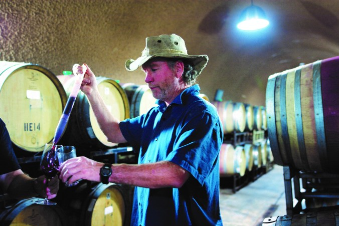 Alex MacGregor using a wine thief, a glass tube that acts like a baster, to put drawn wine into a glass for tasting.