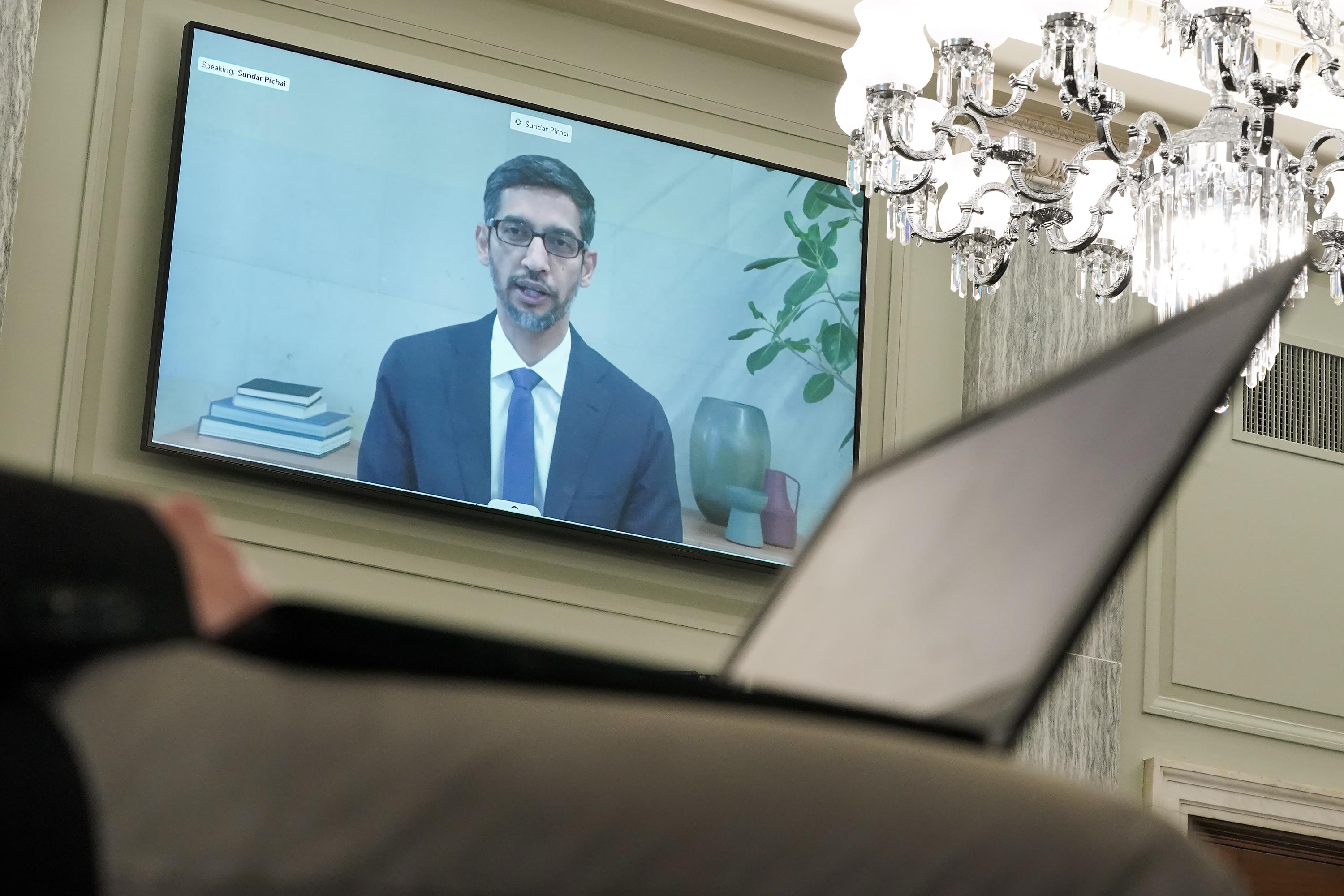 A person with a laptop is in the foreground while Sundar Pichai is on a large screen on the wall.