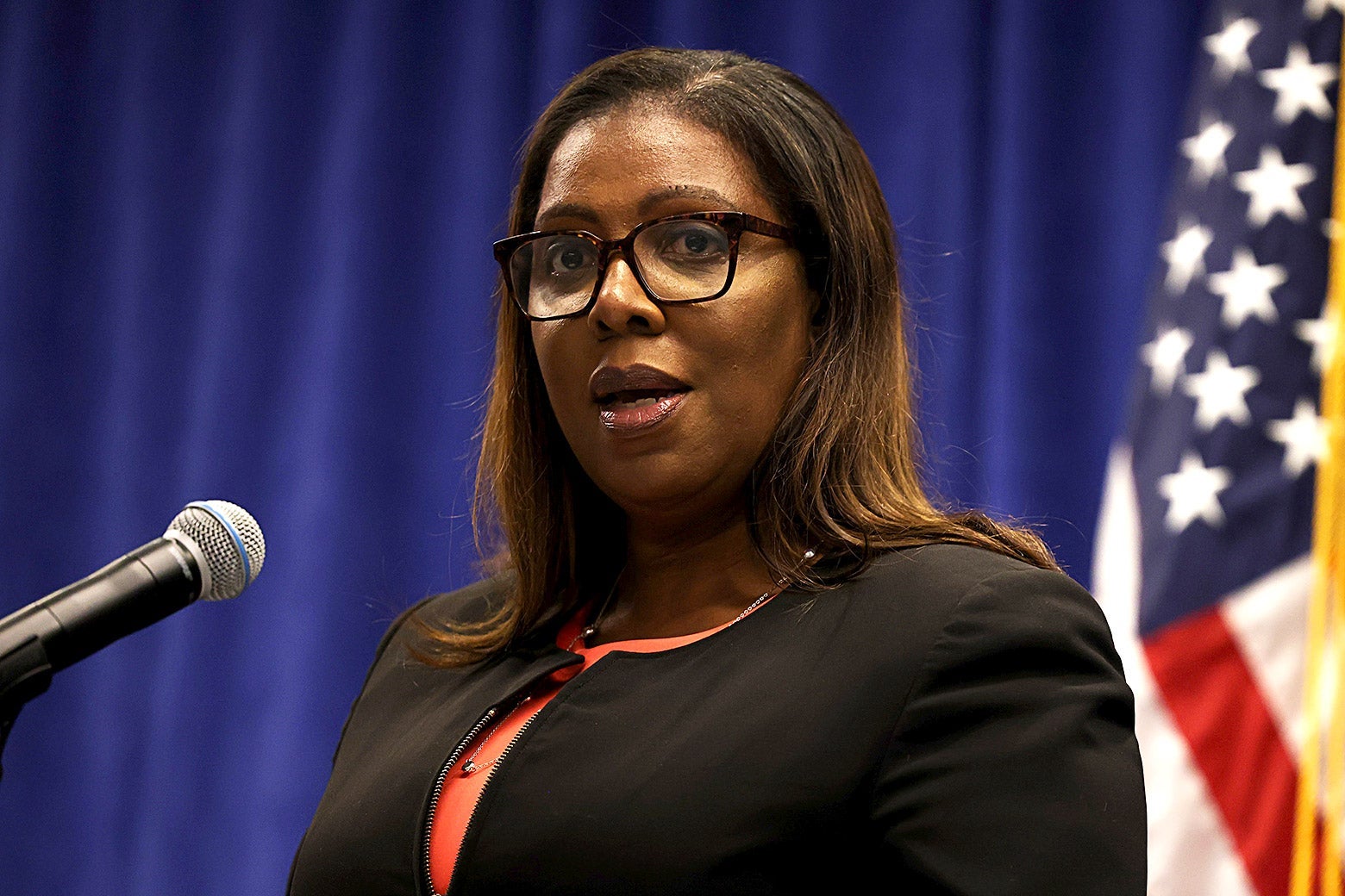 Letitia James speaks into a microphone with an American flag behind her.