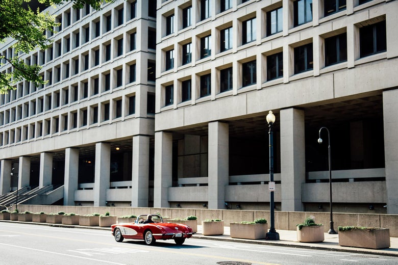 An old-fashioned convertible drives by the FBI headquarters.