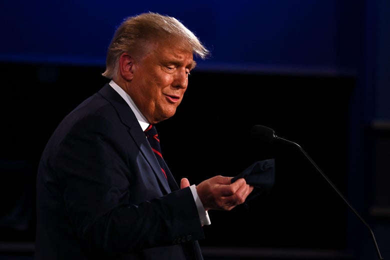 Trump makes a smirky face while holding a face mask and speaking at a lectern.