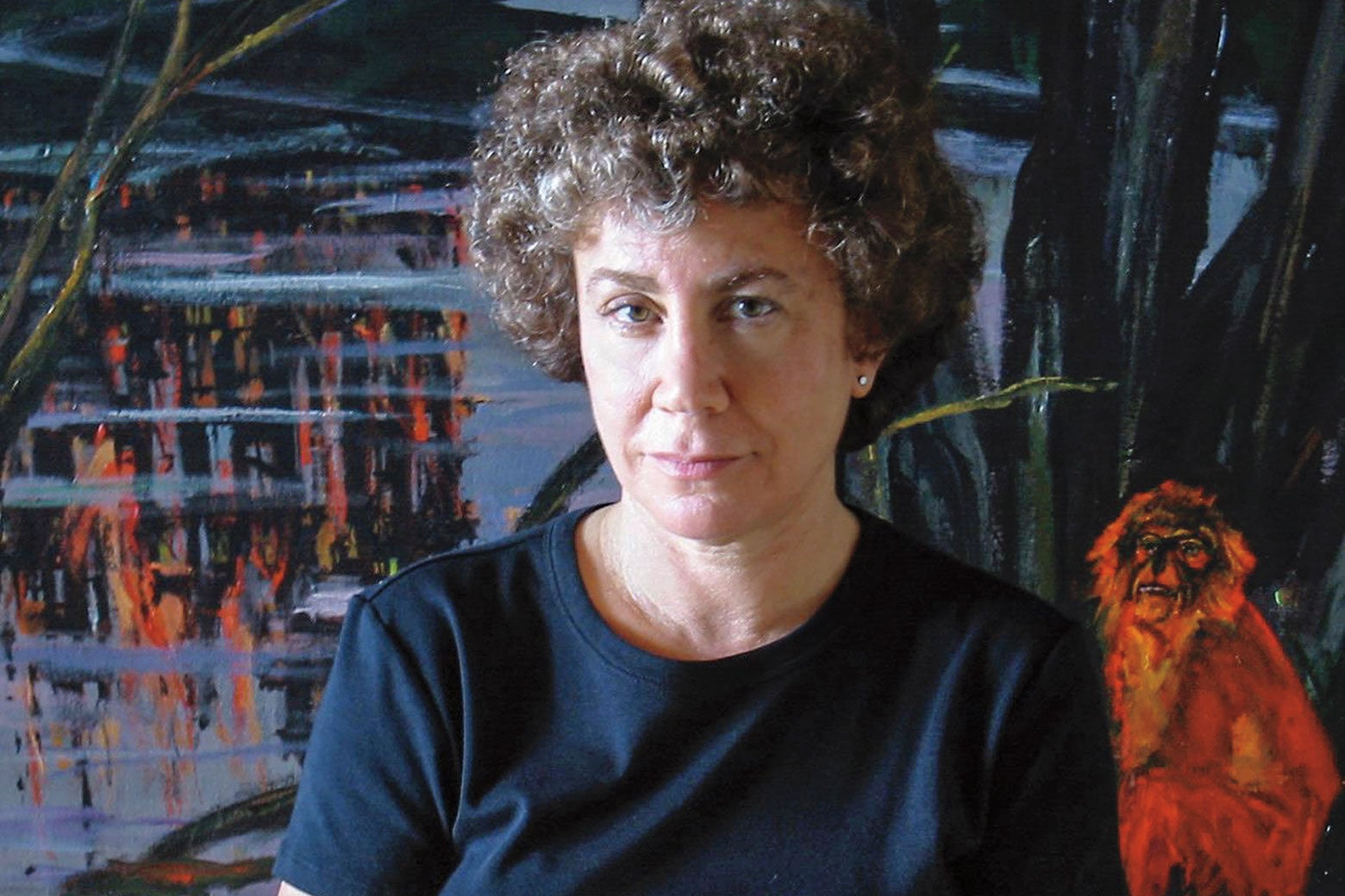 Jill has short curly hair and is not smiling as she is photographed in front of a large dark painting with bright monkeys in it.