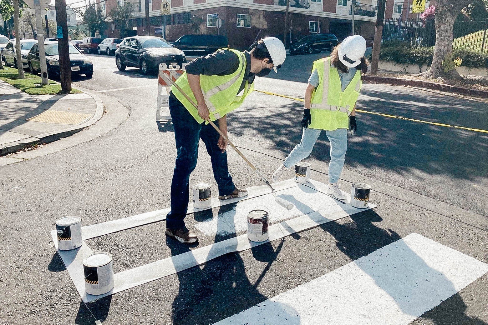 Two activists in yellow suits painting a crosswalk at an intersection