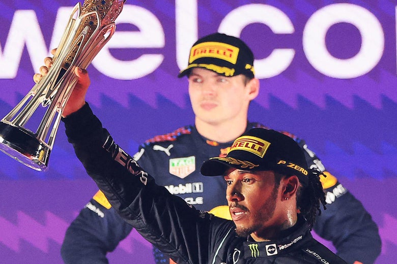Foreground: Hamilton hoists his trophy and looks at the crowd. Background: Verstappen looks on, angry.