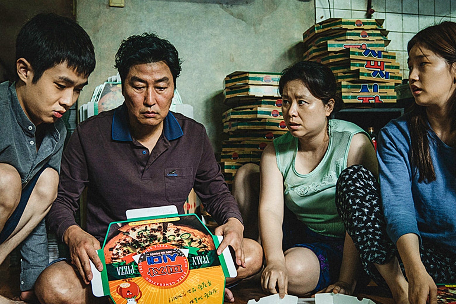 In a scene from Parasite, the Kim family gathers on the floor, surrounded by pizza boxes.