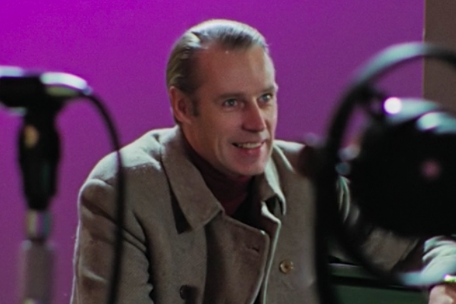 Smiling man in a peacoat with studio mic in the foreground