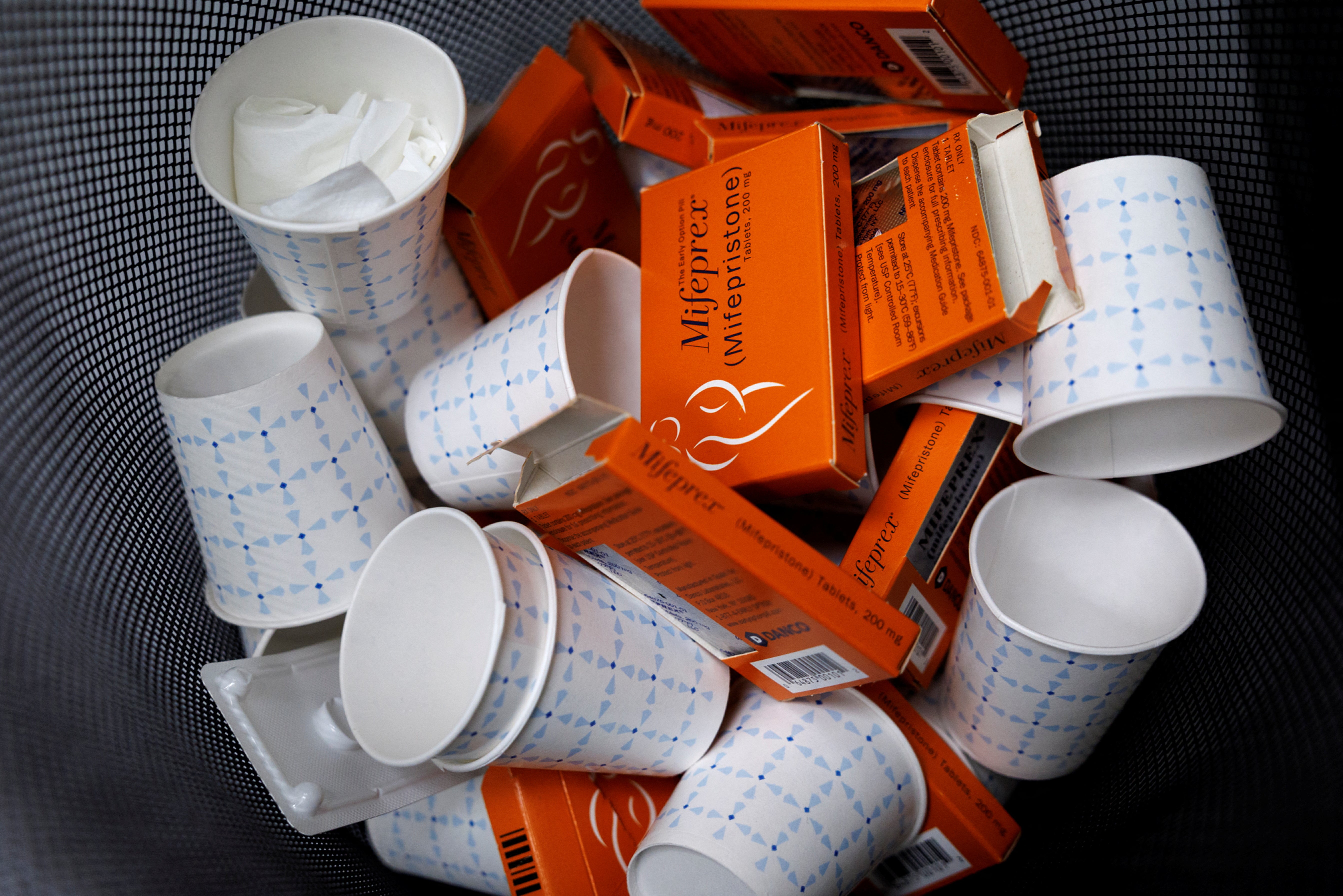 Empty mifepristone boxes and paper cups fill a trash can
