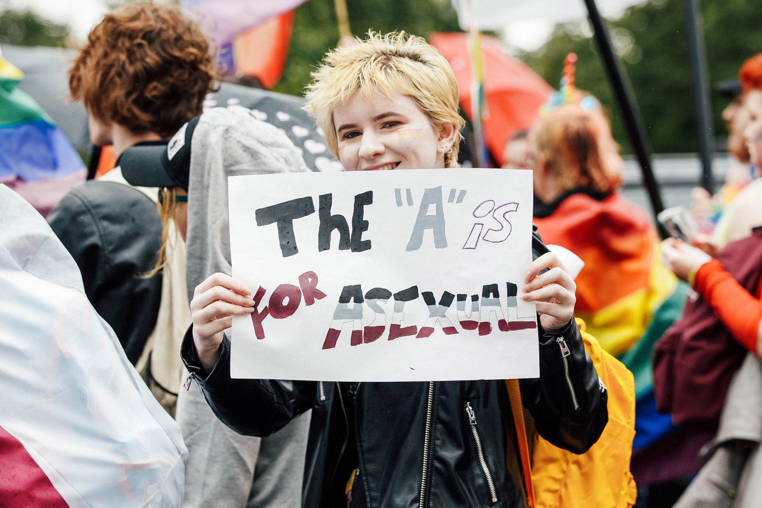 A marcher in a black leather jacket holds a sign that says, “The ‘A’ is for asexual.”