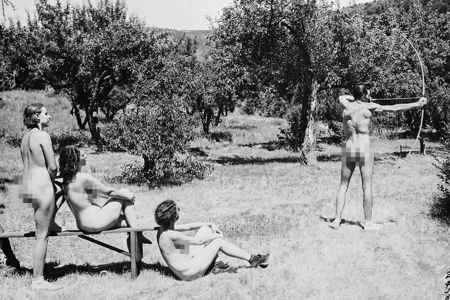 A vintage black and white photo of nudists doing archery.