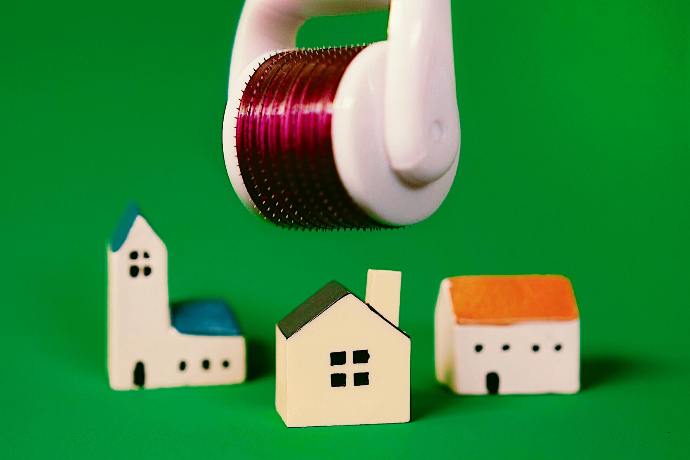 Photo illustration of an Ora Microneedle Face Roller System above toy houses.
