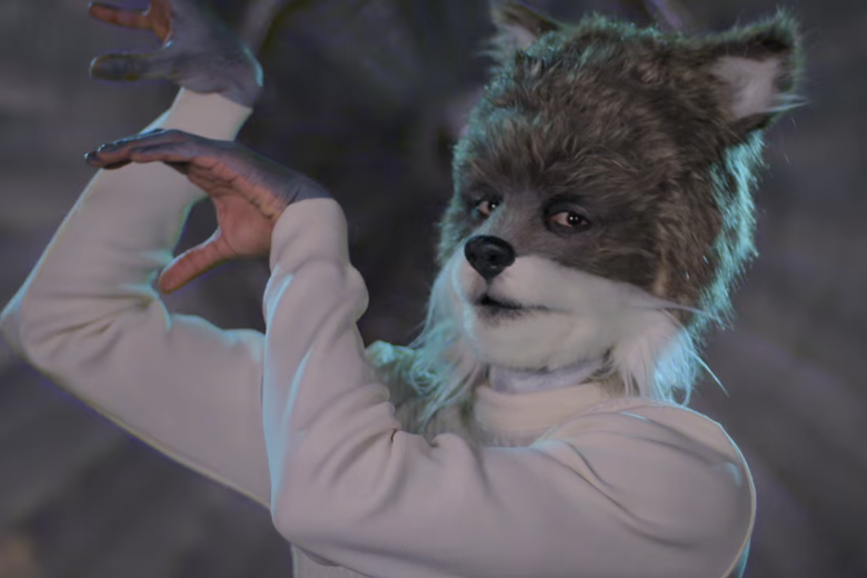 A man in white sweater with his hands up and wearing a wolf head.