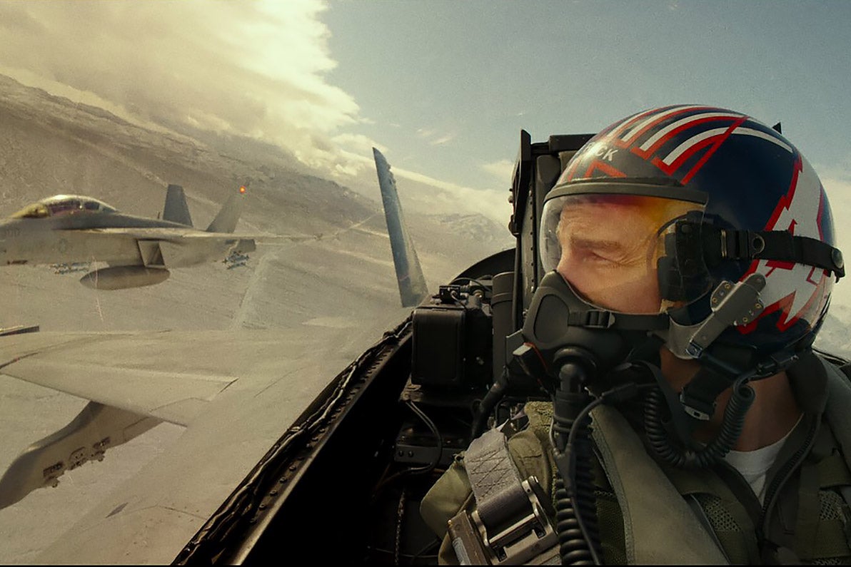Tom Cruise in a fighter jet looking out to his right side as other jets scramble beside him.