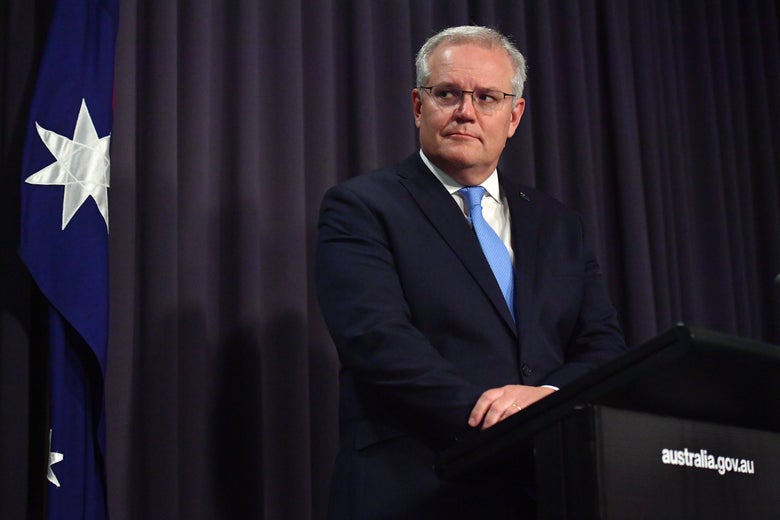 Morrison looks pensively to the side with an Australian flag behind him. 