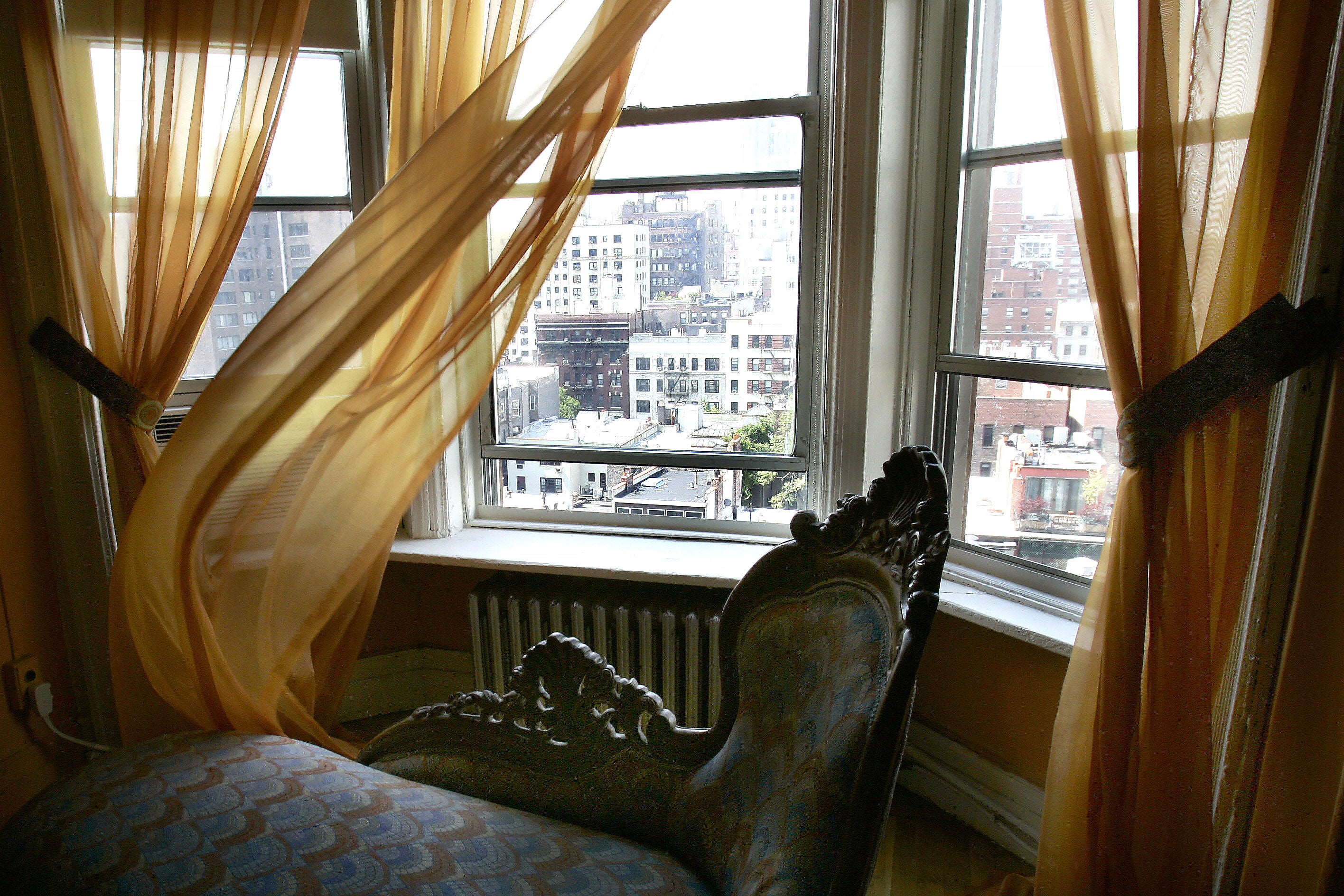 A room in the Chelsea Hotel overlooking the city and the curtains pulled to the side.