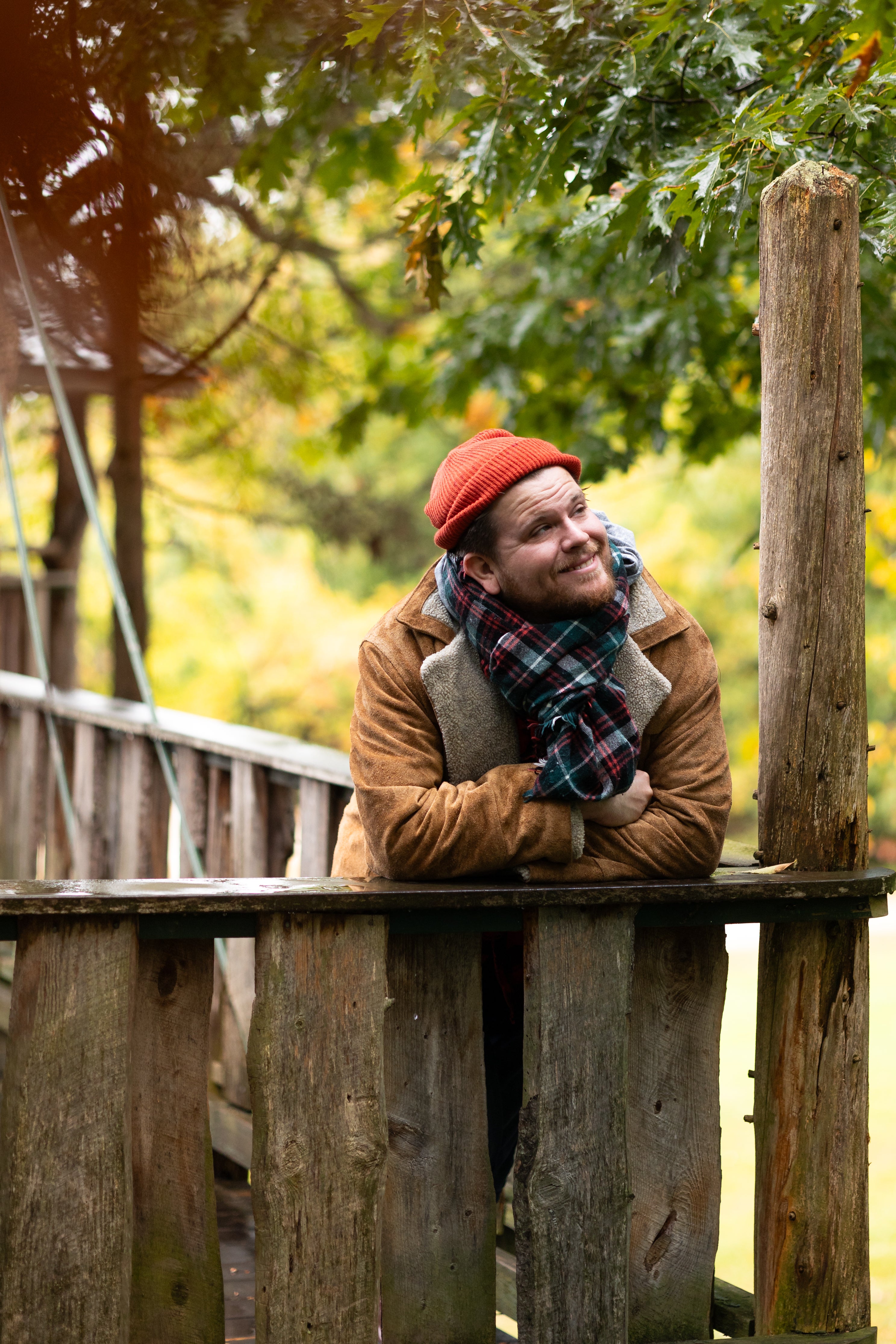 Luke, wearing a beanie, leans against a wooden rail and looks upward, smiling faintly.