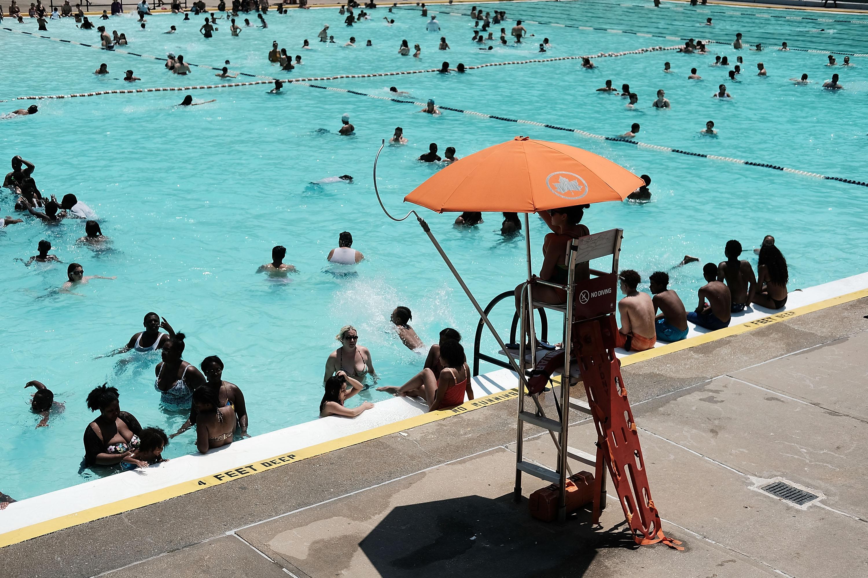 A swimming pool filled with people with a lifeguard looking on.
