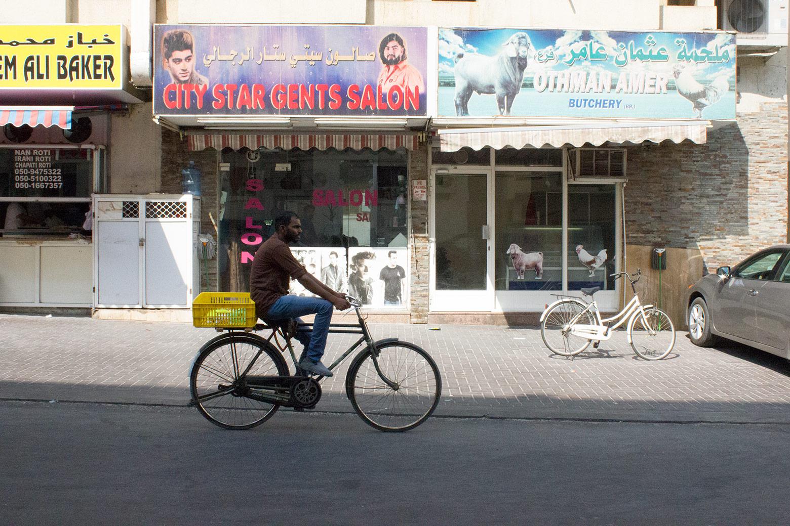 A man rides a bicycle past storefronts in Al Hamriya.