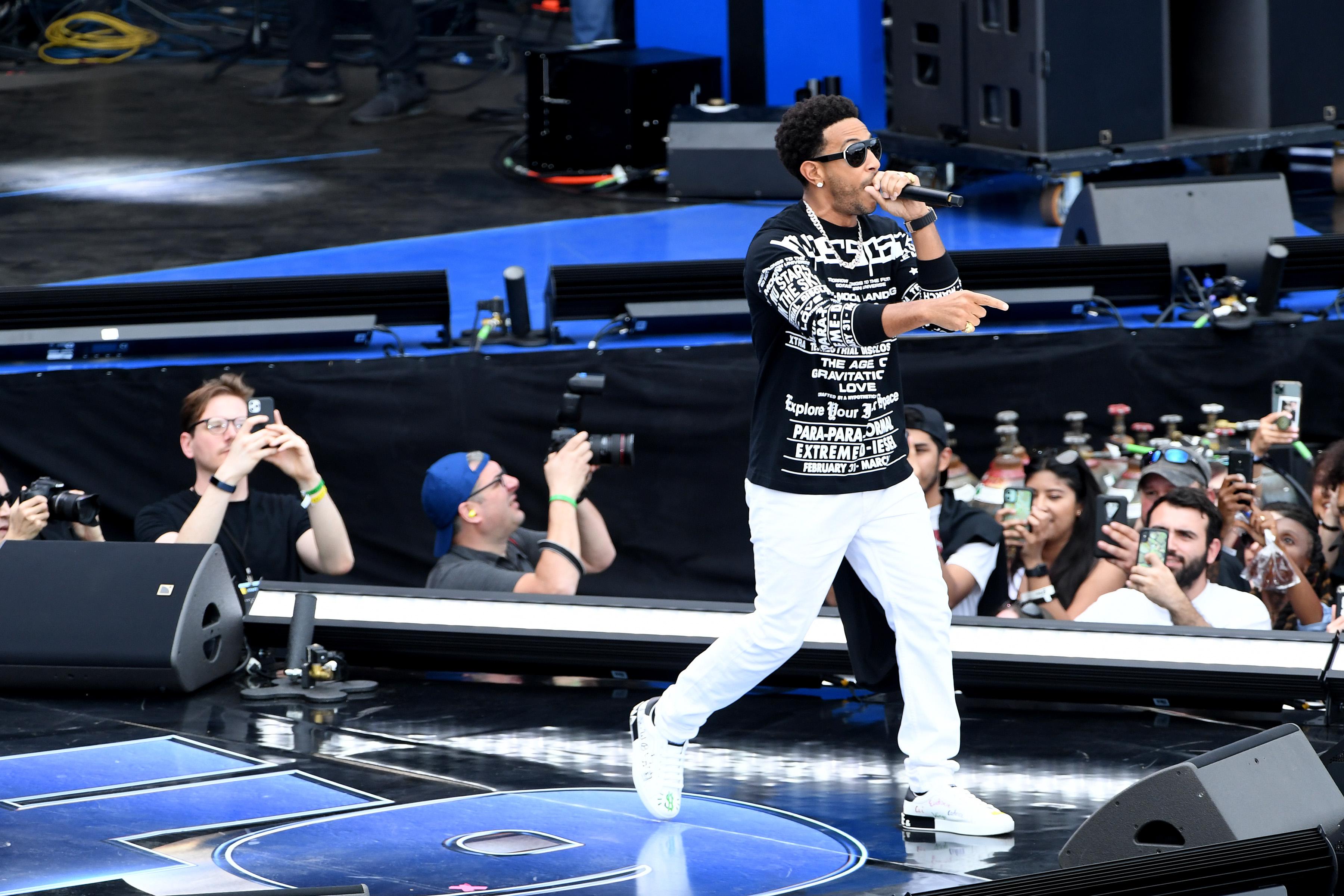 Ludacris holds a mic onstage as fans below him film with their phones