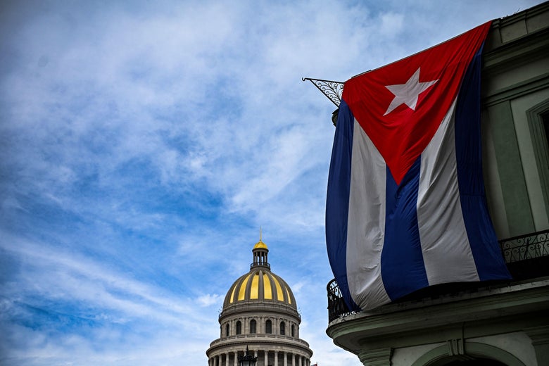 A huge Cuban flag hanging on a building with the dome of the Havana Capitol in the distance.