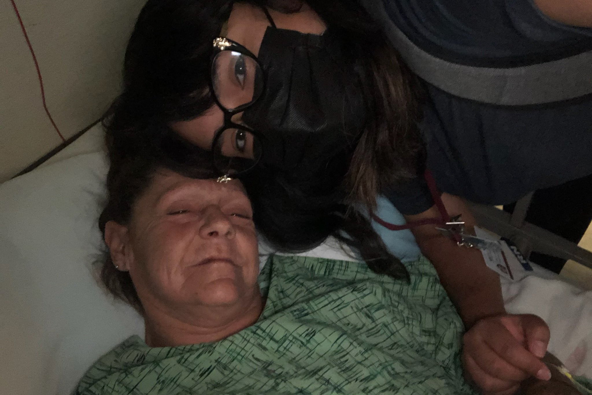 A masked nurse leans close to Denise, who is lying in a hospital bed.