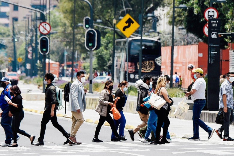 People walk across a crosswalk in Mexico City while wearing masks.