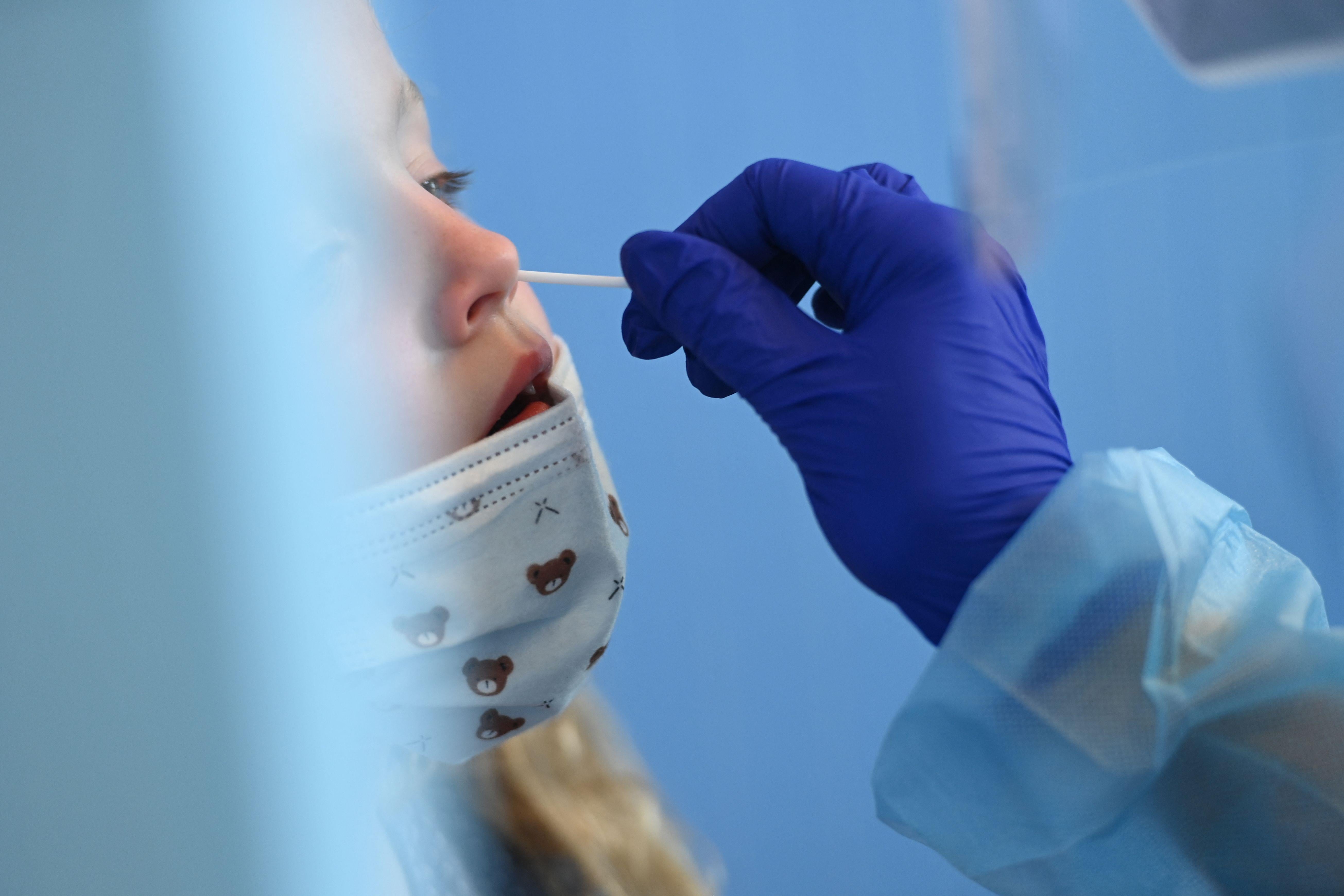A girl leans her head back as a gloved hand sticks a swab up her nose.