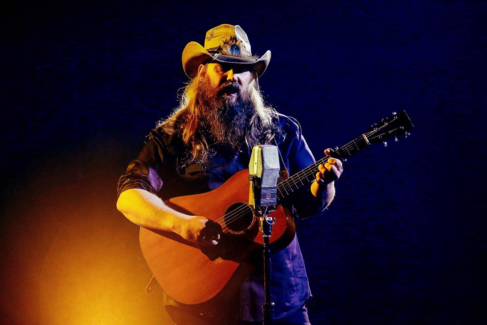 Chris Stapleton holding a guitar and singing into a microphone.