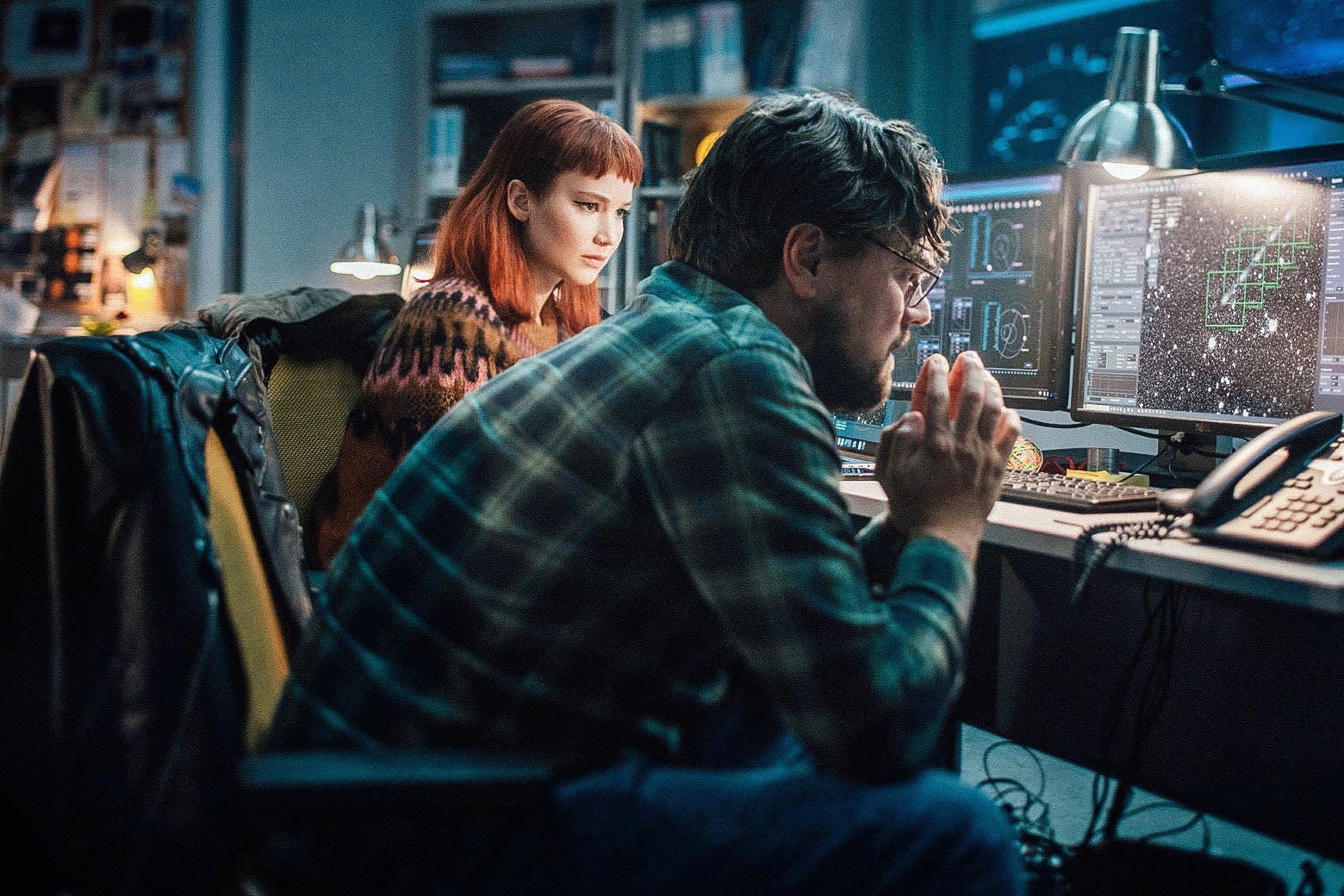 A man and a woman sitting in a dark room looking intently at computer screens showing a comet approaching Earth