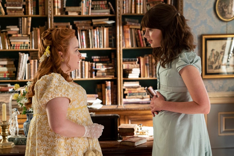 Nicola Coughlan as Penelope Featherington and Claudia Jessie as Eloise Bridgerton stand facing one another in front of a desk and bookshelf.